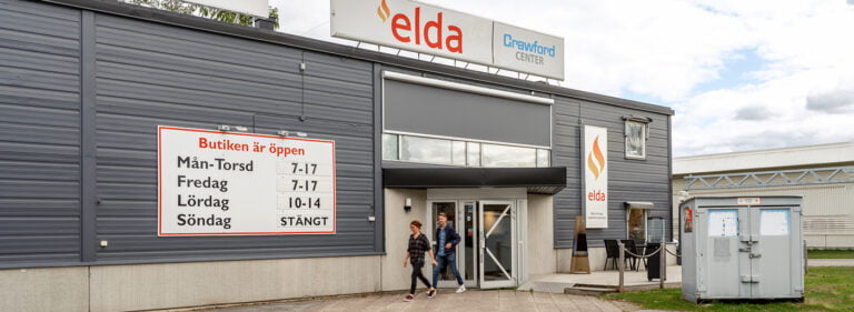 Grå byggnad med skyltar för Elda och Crawford Center. Öppettider syns på en stor skylt. Två personer går ut genom entrédörren.