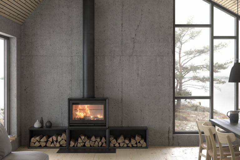 Modern kamin i betongrum med brinnande ved, omgiven av stora fönster som visar en naturskön utsikt. Vedstapel och inredning i skandinavisk stil.