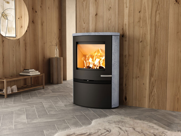 Modern kamin i ett stilrent rum med träpaneler och grått klinkergolv, brinnande eld synlig genom glasdörren.