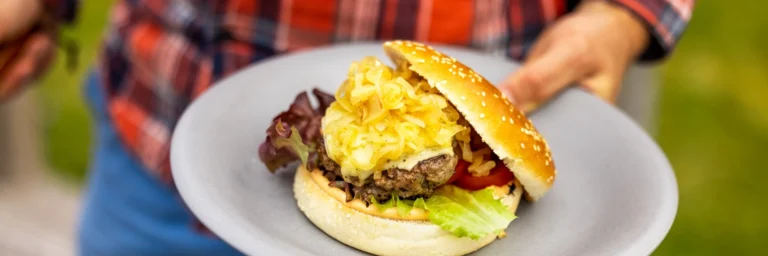 En saftig hamburgare med sallad, tomat och karamelliserad lök på en sesambulle serveras på en grå tallrik.