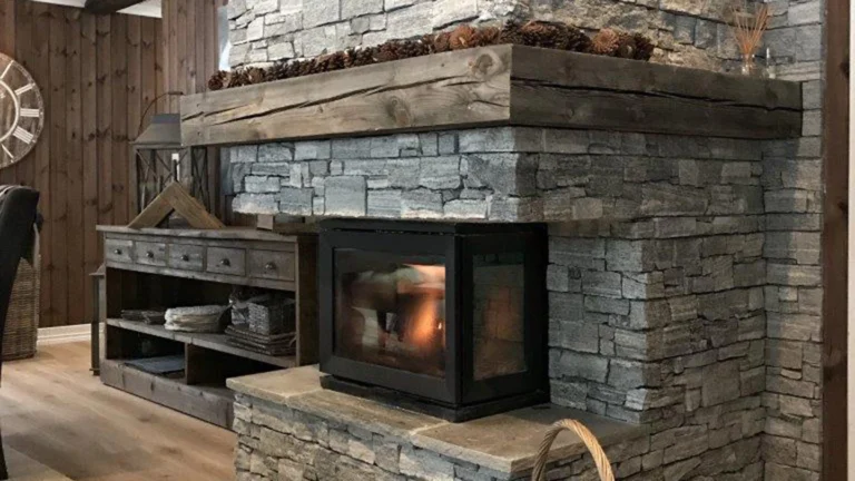 Rustik eldstad i sten med trädetaljer och brinnande ved. Intill syns ett träbord med olika dekorationer. Hela rummet har en varm och inbjudande atmosfär.