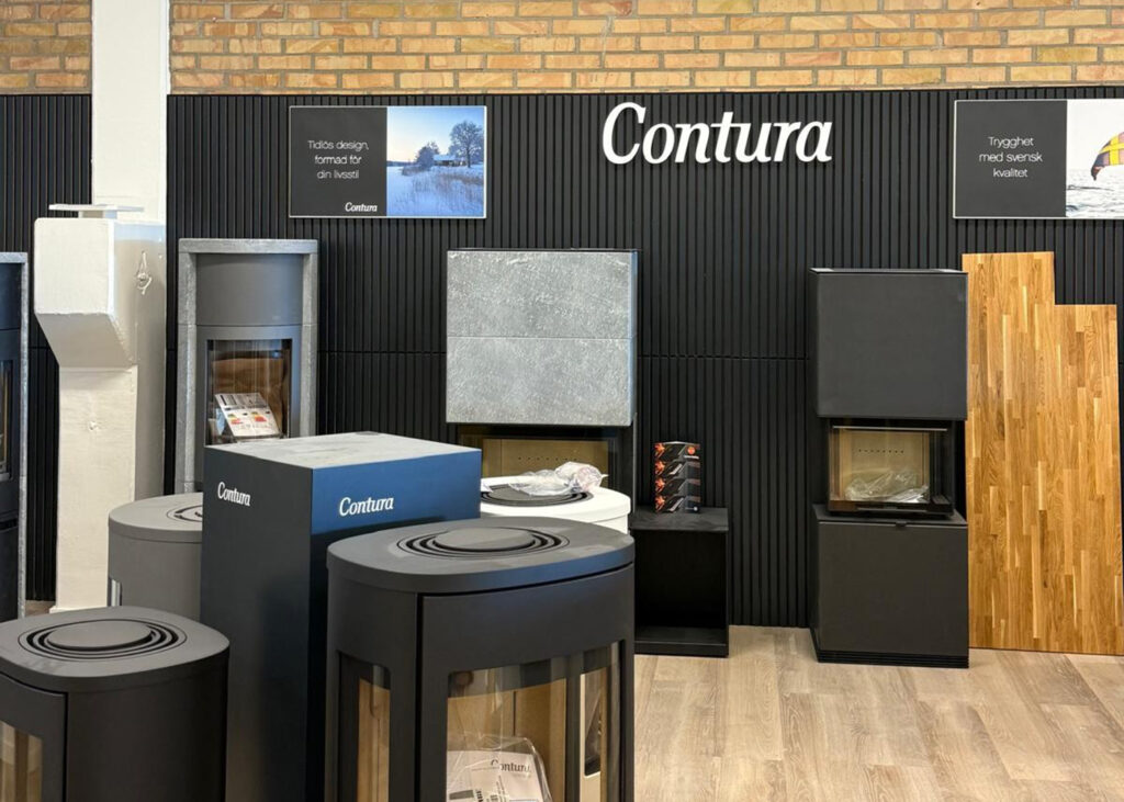 Utställning av Contura kaminer i en butiksmiljö med svart väggpanel och trädetaljer. Kaminerna står på trägolv, med skyltar för design och kvalitet.