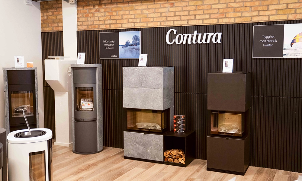 Utställning av Contura-kaminer i en butik, med fyra olika modeller uppställda mot en vägg. Bakgrunden har en tegelvägg och skyltar med information.