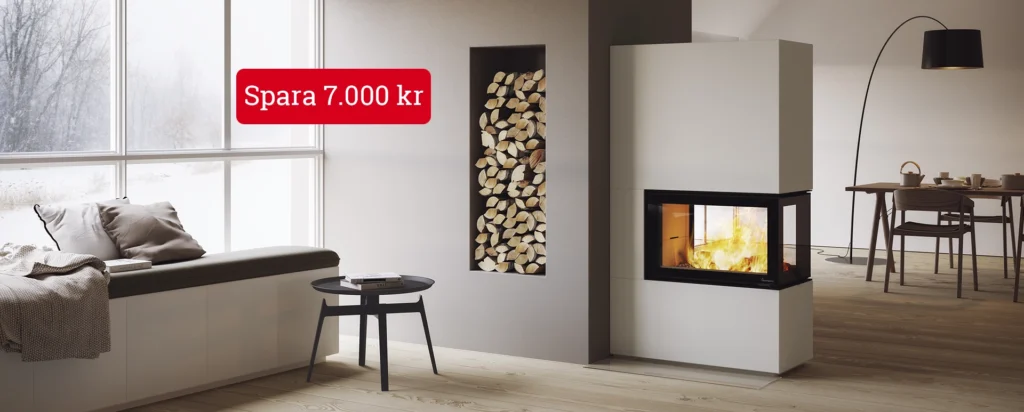 Modern vardagsrum med braskamin, vedförvaring och stora fönster med vinterutsikt. Text: "Spara 7.000 kr". Mysig inredning med bord, stolar och golvlampa.