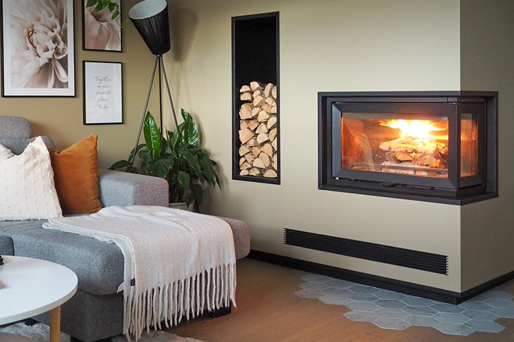 Modernt vardagsrum med grå soffa, väggmonterad kamin och vedförvaring. Växter och konstverk på väggen skapar en inbjudande atmosfär.