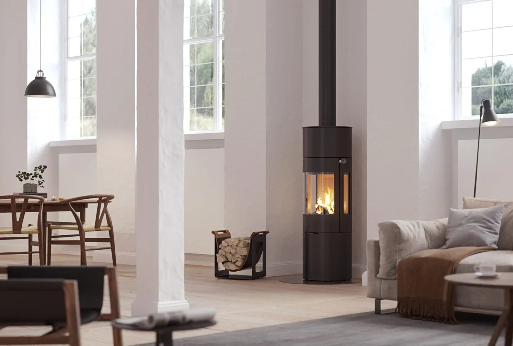Modernt vardagsrum med stilren kamin och vedställ. Ljus inredning med stora fönster, matbord och soffgrupp. Mysig atmosfär med fokus på kaminens eld.