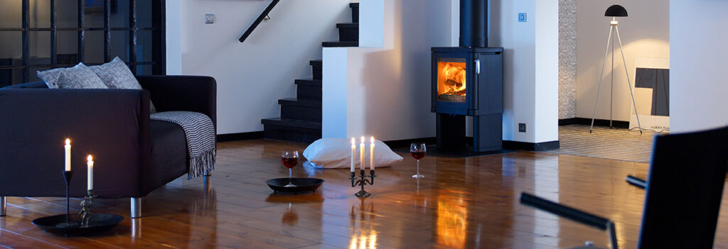 Modernt vardagsrum med braskamin, soffa, tända ljus och vinglas på trägolv. Mysig atmosfär med elegant inredning och varm belysning.