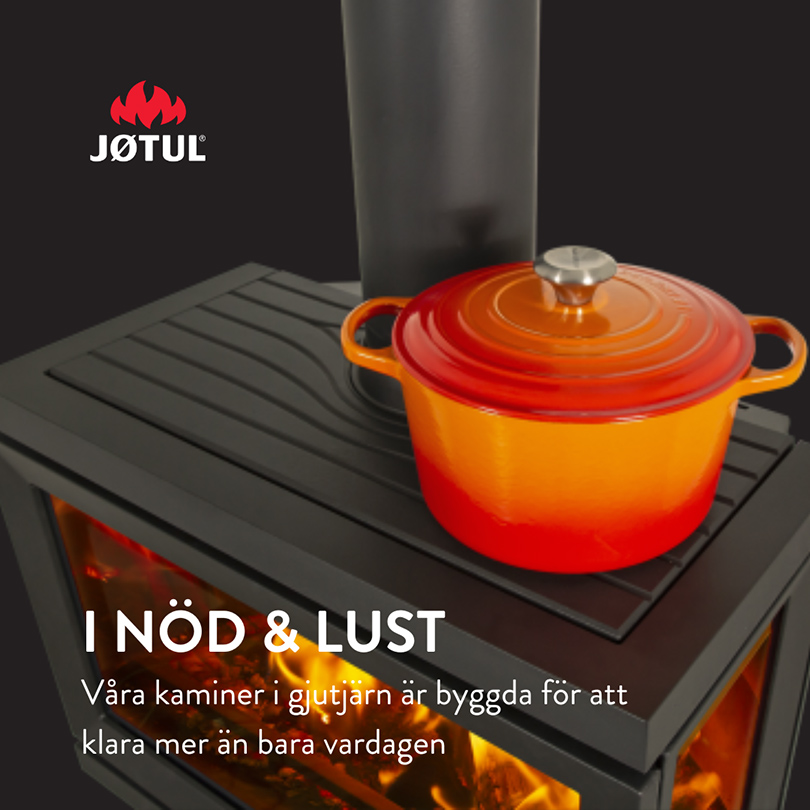 Eldstad med orange gjutjärnsgryta ovanpå, Jøtul-logotyp och texten "I NÖD & LUST" synlig. Visar eldstadens hållbarhet och design.