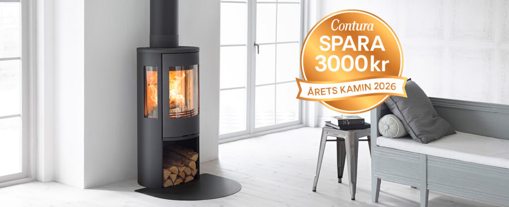 Modern kamin i svart med brinnande ved, placerad i ljust vardagsrum. Kampanjskylt om 3000 kr rabatt och utmärkelse "Årets kamin 2026" synlig.
