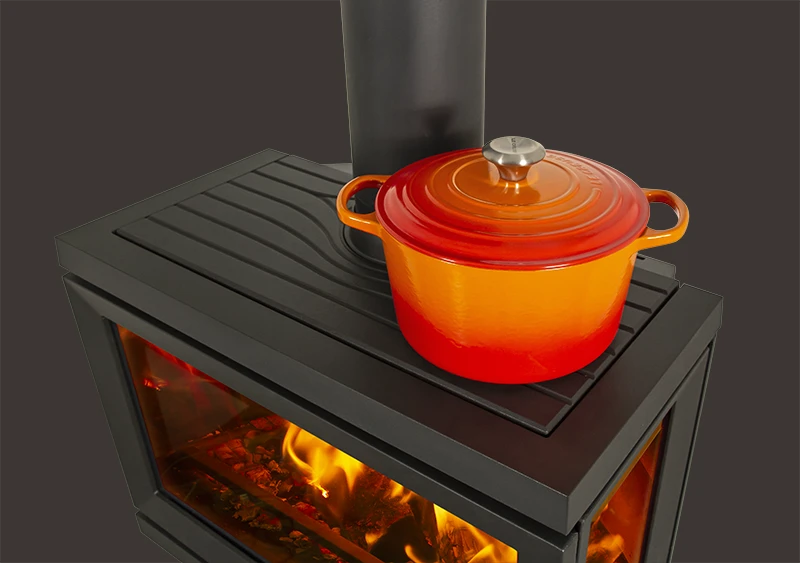 Röd emaljerad gryta på svart vedkamin med synlig eld inuti.