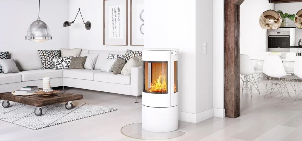 Modernt vardagsrum med vit kamin, grå soffa och rustikt soffbord. I bakgrunden syns ett kök med vita stolar och trädetaljer.