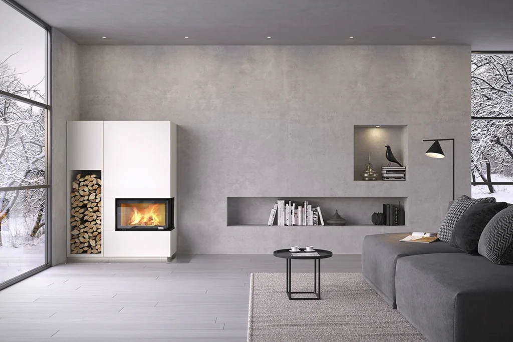 Modern vardagsrum med grå soffa, svart sidobord och väggmonterad vit kamin med eld. Stora fönster visar snötäckt utsikt. Minimalistisk inredning med böcker och prydnader.