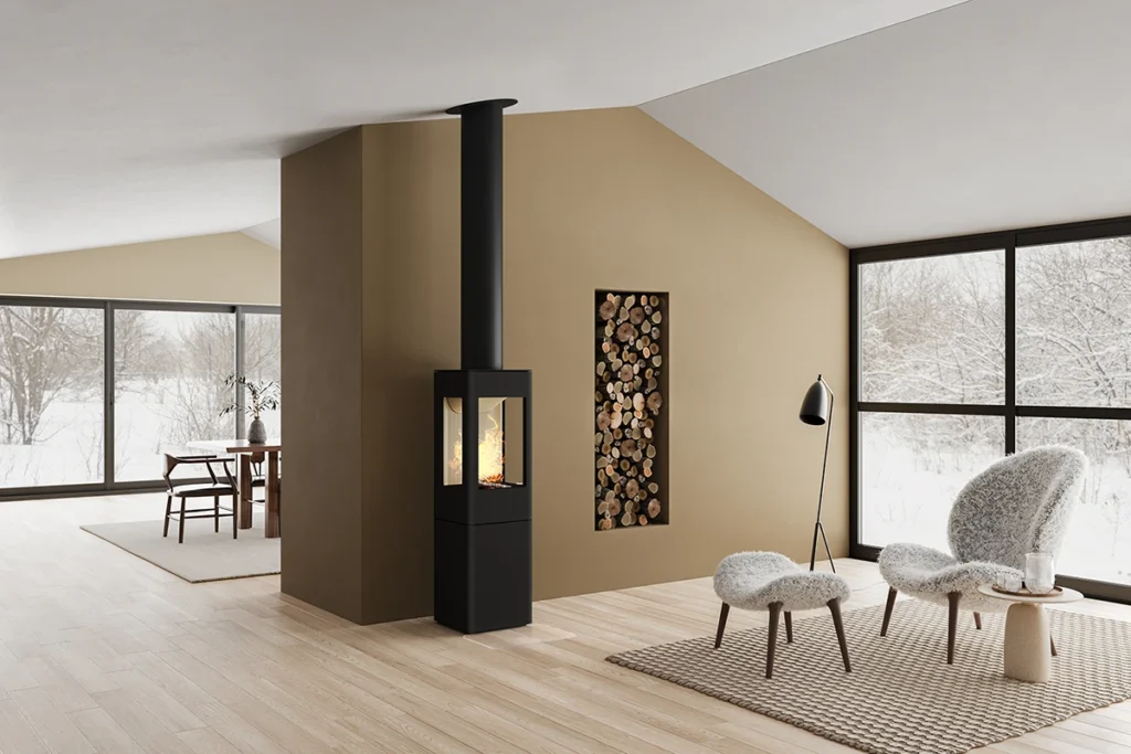 Modern vardagsrum med svart kamin, vedförvaring, och stora fönster som visar snölandskap. Två fåtöljer och en lampa står på en matta av naturmaterial.